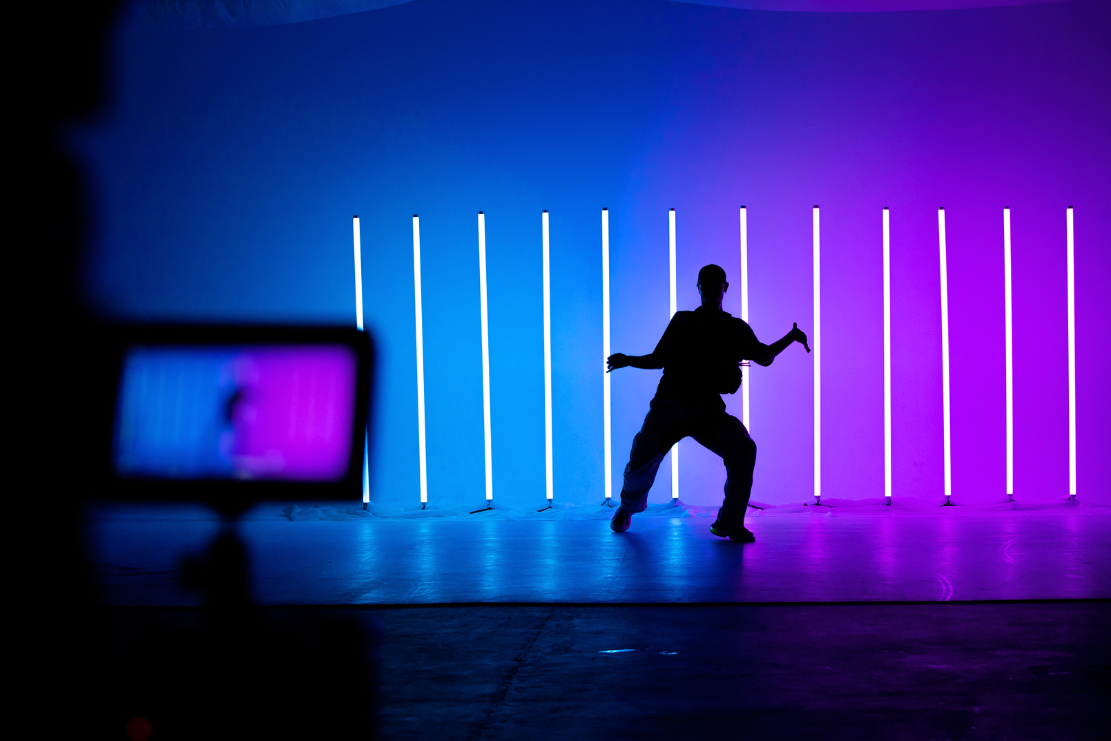 Camcorder display and blurred frame with young guy dancing street dance hip hop in a studio with neon lighting tube on a colorful background