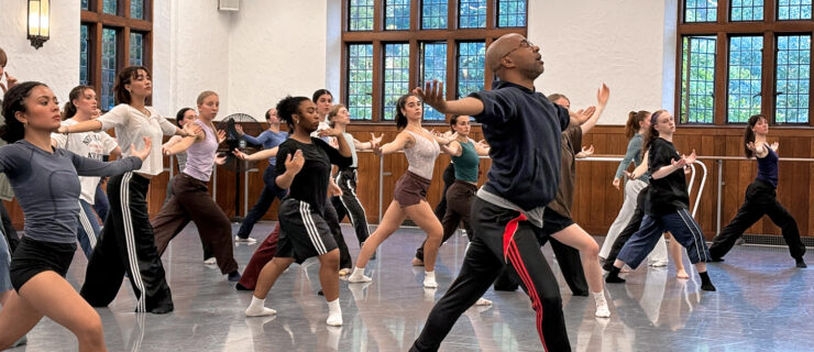 Matthew Rushing leads a group of students in the studio. He lunges in 4th position with both arms opening side.