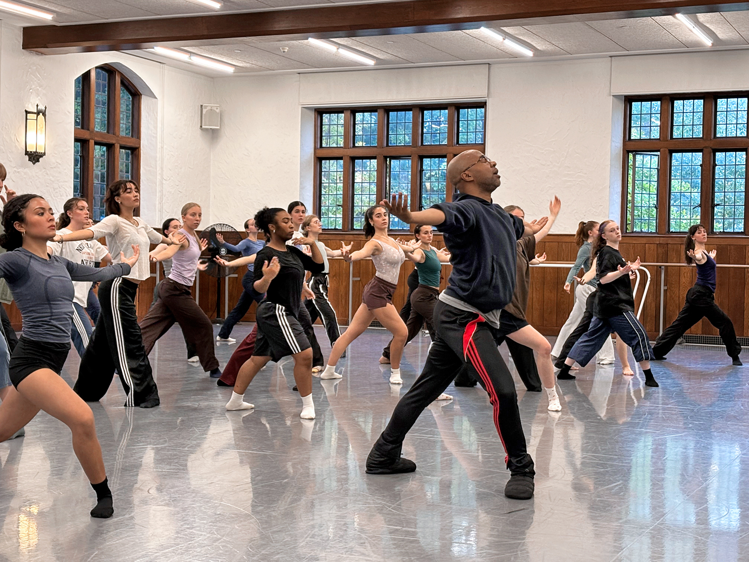 Matthew Rushing leads a group of students in the studio. He lunges in 4th position with both arms opening side.