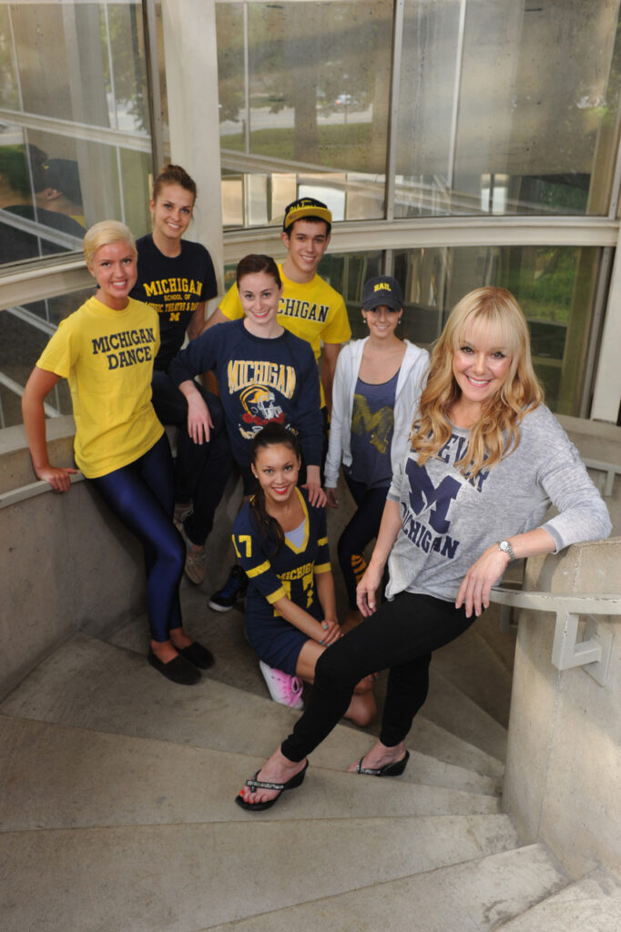 Rice, her long blonde hair loose, stands on a staircase with six young dancers, all wearing UMich gear.